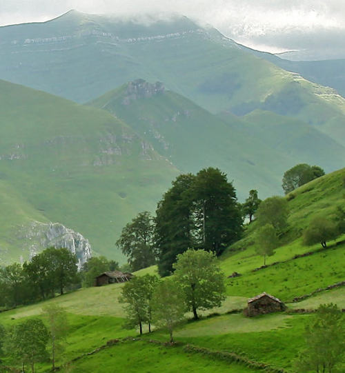 Paisaje de Valles Pasiegos con cabañas pasiegas de madera y piedra entre prados verdes y montañas en Cantabria